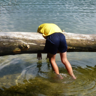 müdes Kind steht im Wasser beugt sich über umgestürzten Baumstamm